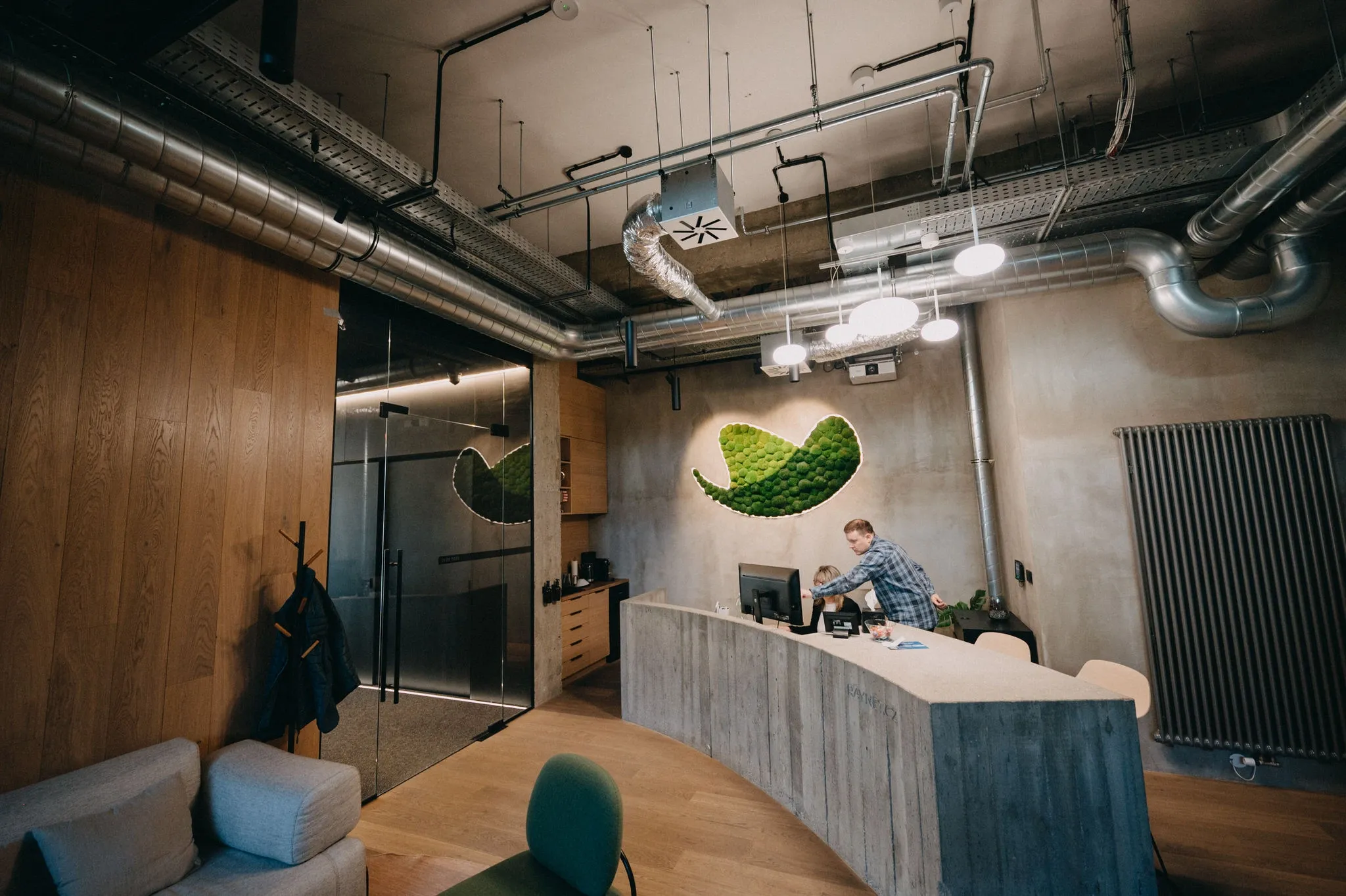 Modern office reception featuring a person at a curved desk and large green moss art.