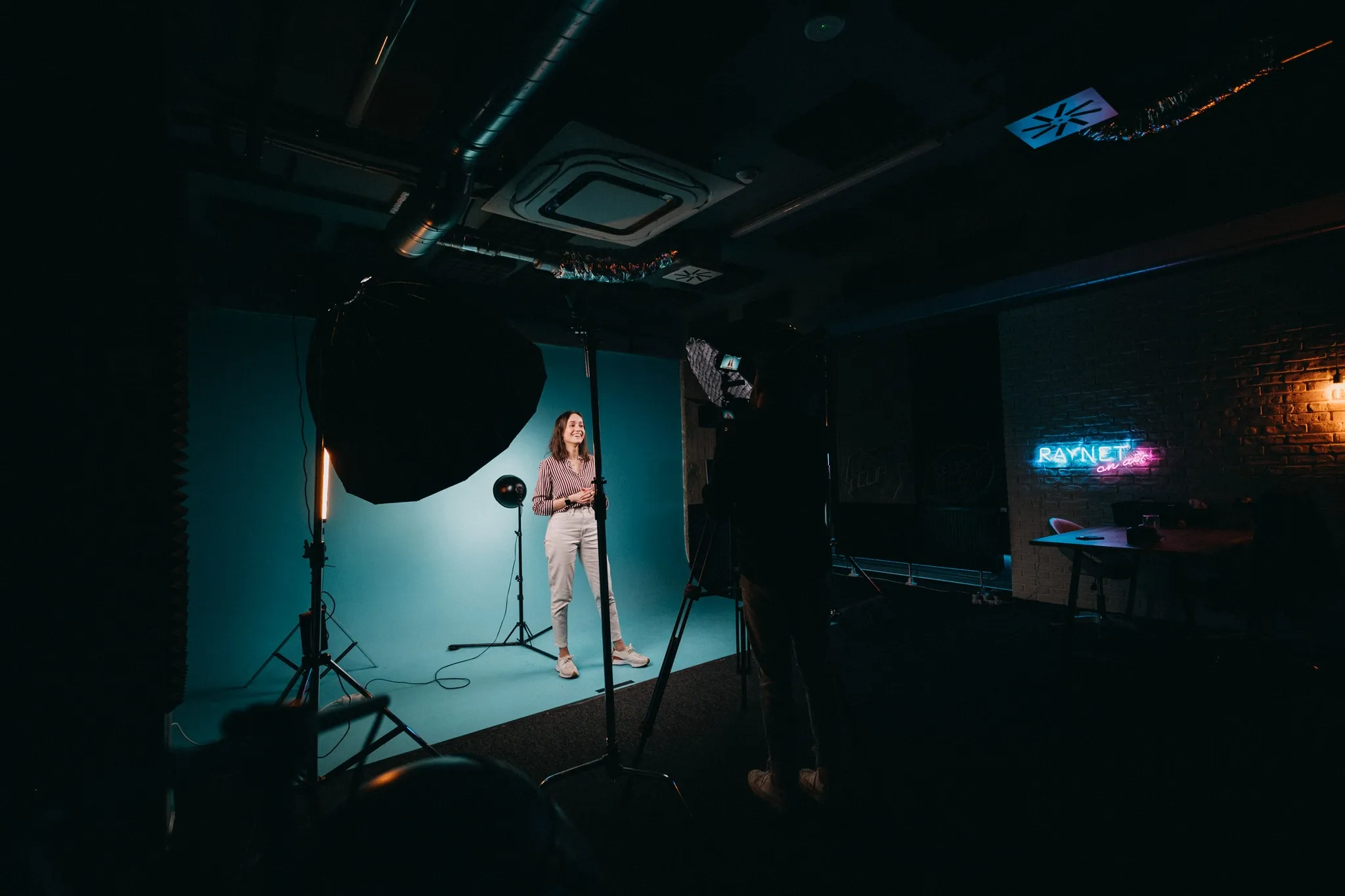 Woman stands in a dark studio, illuminated by softbox lights, posing for a shoot.