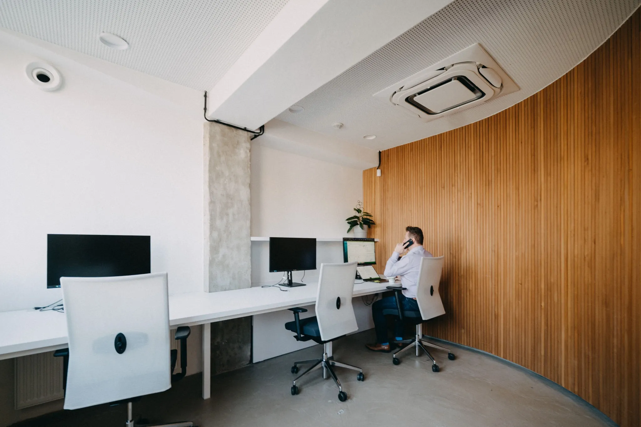 Person talking on phone at a desk with computers in a modern office with wooden wall.