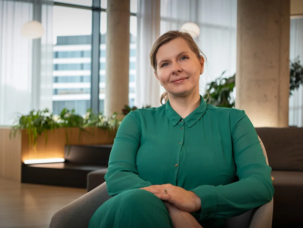 A smiling woman in a green dress sits comfortably in a modern office lounge.