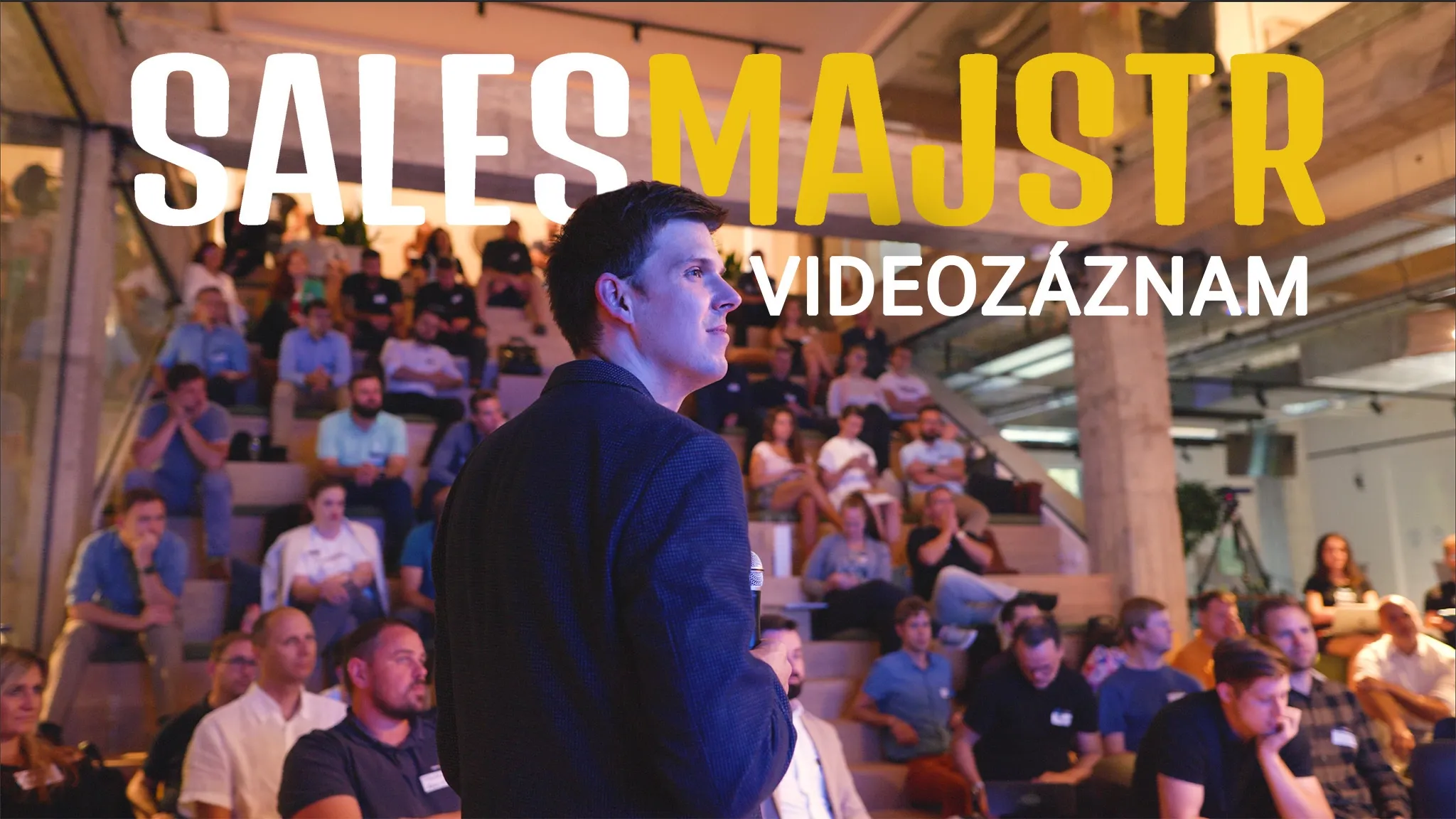 Man speaking to a large audience at an event with 'SALESMAJSTR VIDEOZÁZNAM' text.