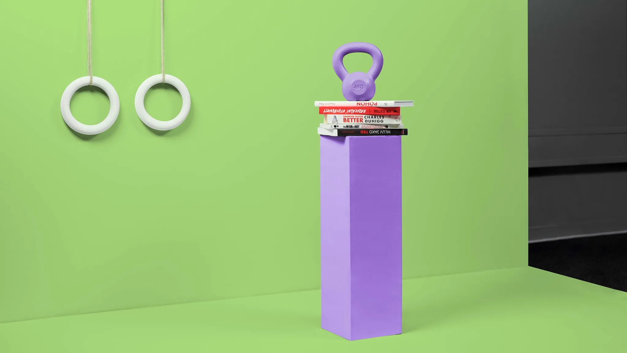 Gymnastic rings, a purple pedestal with stacked items, and a kettlebell against a green wall.