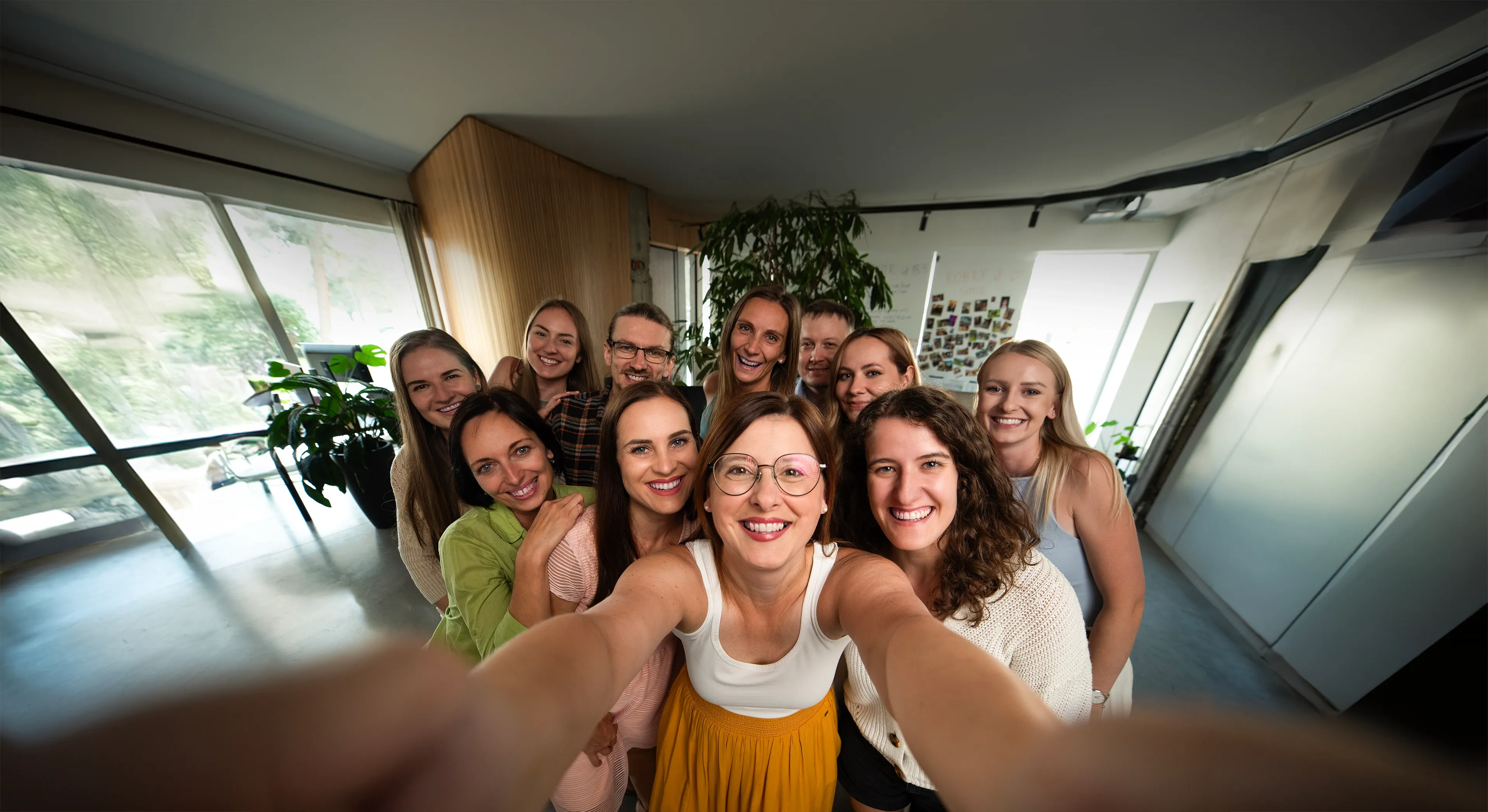 A large group of smiling women happily pose for a low-angle selfie indoors.
